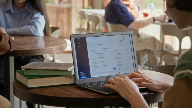 Girl taking online test on laptop in cafe, typing answers on educational platform. Footage is ideal for marketing e-learning platforms, online courses, and digital schools