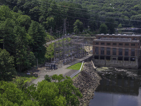 Aerial view of the Stevenson Generating Station with its brick hydroelectric powerhouse, electrical substation, and steel structures, set along a riverbank in Monroe, CT, United States.