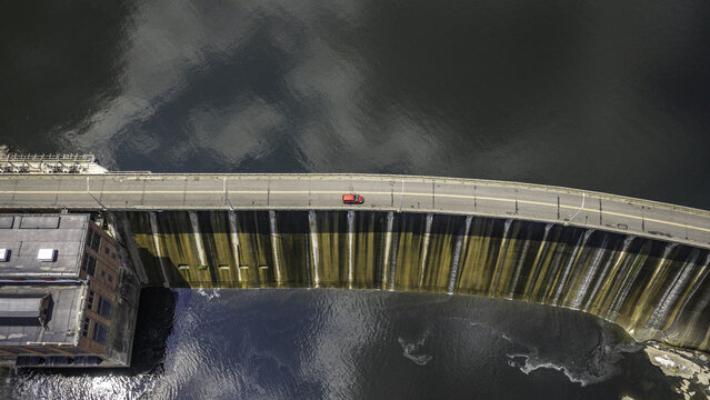 Aerial view of Stevenson Dam with a red car driving across the road atop the hydroelectric powerhouse structure in Monroe, CT, United States.