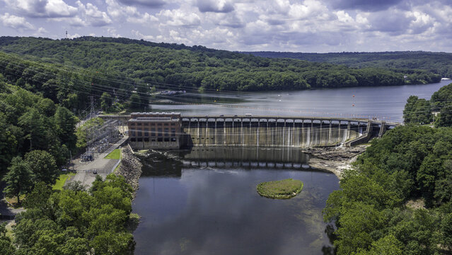 Aerial view of the Stevenson Generating Station hydroelectric dam and electrical substation, with a brick power plant, concrete dam, and surrounding lush forest in Monroe, CT, United States.