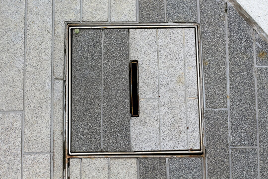 Granite paving stones with a metal drain cover and grate on a city sidewalk