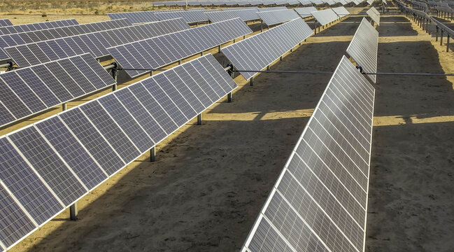 Aerial view of a utility scale photovoltaic solar farm with single axis tracking panels arranged in rows across flat desert terrain in Antelope, California, United States.
