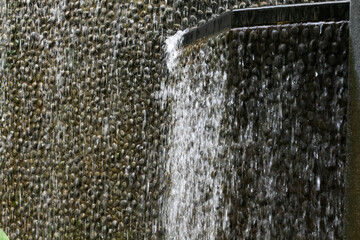 Water cascades down a textured wall of smooth river stones © khomkrit