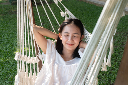 Relaxed woman resting in a hammock outdoors with eyes closed, enjoying peaceful nature, wellness, self care, stress relief, leisure, mindfulness, relaxation, and healthy lifestyle.