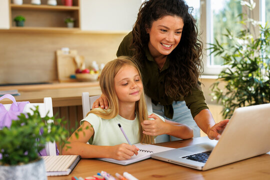 Mother helping her daughter studying online learning new skills and doing homework with a laptop at the kitchen table
