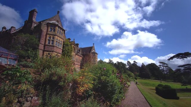 Victorian High Gothic revival facade of Knightshayes Court framed by vibrant purple flowers in the estate gardens, photographed in Tiverton, Devon, England, on 24.08.2024.
