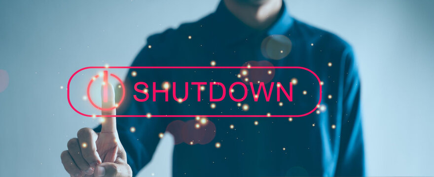 Hand taps glowing "SHUTDOWN" button on holographic screen. Soft bokeh lights surround the action. Businessman gestures to activate digital command. Futuristic interface implies control or pause