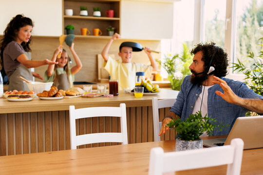 Dad trying to work remotely from the kitchen during a video call while his kids and wife are creating chaos in the background