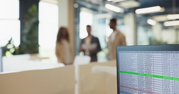 Office team colleagues meeting in discussion. A monitor displays a spreadsheet with rows of data, while professionals plan strategy in a bright open office. Clear concept of data driven teamwork.