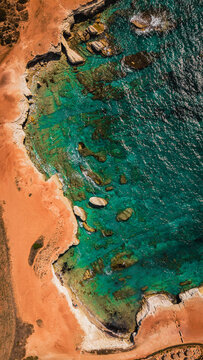 Aerial top down view of rugged rocky coastline and crystal clear sea water.