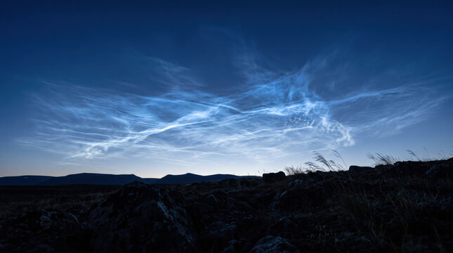 Noctilucent cloud glowing sky night twilight landscape horizon mountain blue glow above dark rocky terrain and grass with serene atmospheric summer scenery