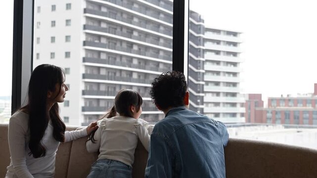 ホテルラウンジの窓際で景色を眺める30代日本人夫婦と6歳の子どもの後ろ姿