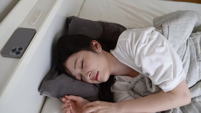 ベッドで寝返りをしながら眠る20代日本人女性