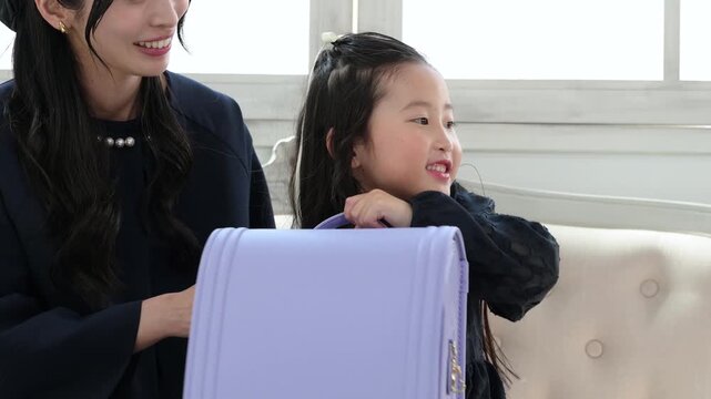 ランドセルを持ってソファで笑顔で会話をする30代の母親と6歳の日本人女の子