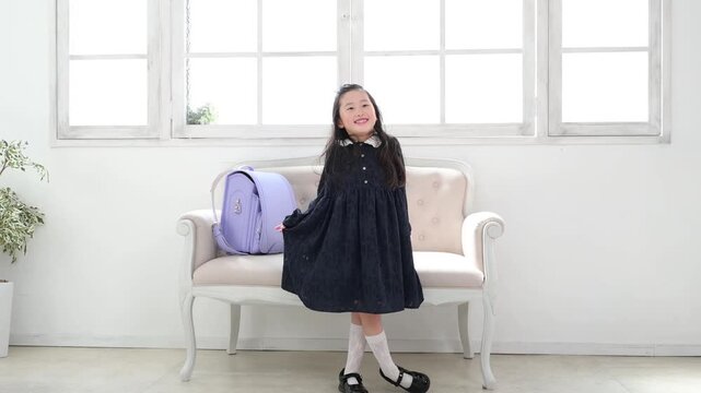 ランドセルをソファに置いてカーテシーをする6歳の日本人女の子