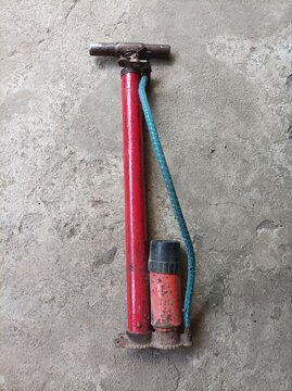 Old red manual air pump with a blue hose on a rough concrete floor.