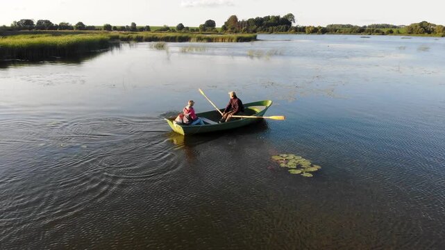 Couple rowing a boat together on a peaceful lake in the countryside at sunset
