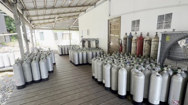 Large reserve of scuba cylinders stored at a dive center in Asia, with special gas tanks, filling equipment and hoses connected to the compressor system.