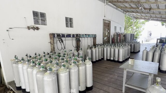 Zoom toward scuba tank filling hoses at an Asian dive center, with rows of cylinders connected to a compressor located behind the wall.