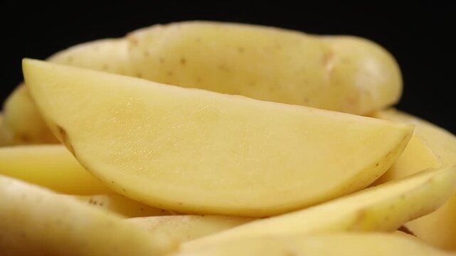 Unpeeled raw potato wedges slowly rotating on a black background