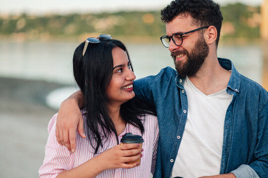 Smiling mixed race couple enjoying outdoor coffee break, embracing happiness and companionship