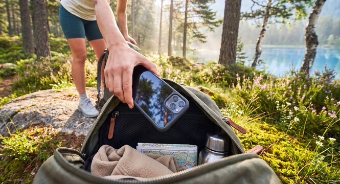 Woman puts her smartphone into a backpack during an outdoor escape by the lake. Digital detox and conscious disconnection from technology concept.