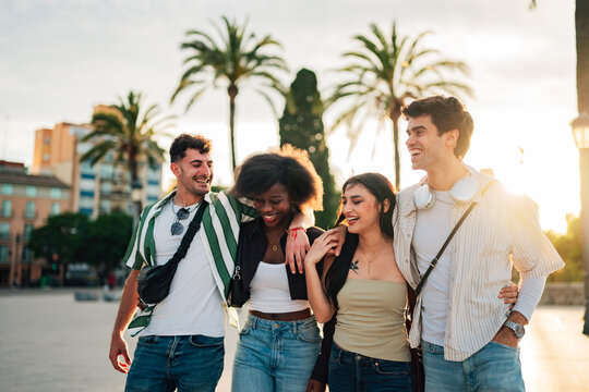 Diverse group of young adult friends walking together and laughing in a city park at sunset