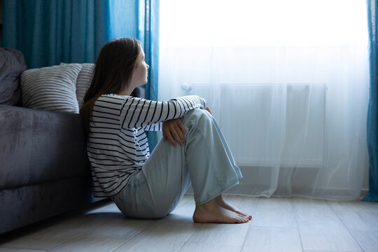 Depressed teenage girl sitting alone at home, feeling sad and overwhelmed, mental health concept