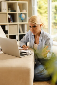 Frustrated woman in casual attire working on laptop at home office