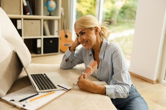 Freelance woman working from home, smiling at laptop, cozy small office setting