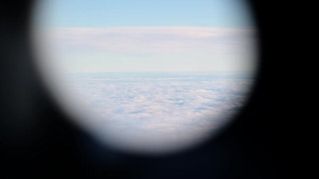 View through an airplane window of a thick layer of white clouds below and blue sky above