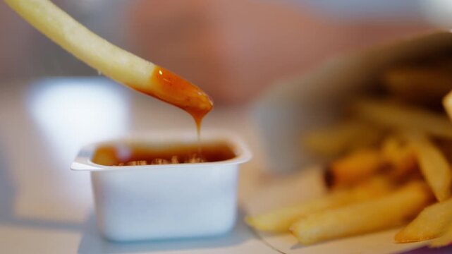 Close-up of hand dipping crispy golden French fry into ketchup, showcasing a popular fast-food snack. Comfort food, casual eating, dipping sauce and restaurant meal concept.