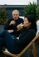 Fototapeta premium Mature couple relaxing outdoors on a rooftop terrace, enjoying refreshing drinks in a casual setting