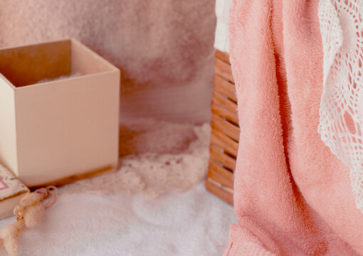 Pink towel, white lace, and pastel box creating a cozy, soft atmosphere, embracing wellness, beauty, and peaceful self-care with calming textures