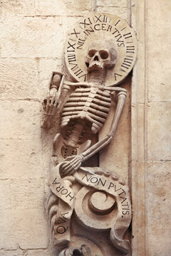 Skeleton on Church of Purgatory (1747), Bitonto, Italy. He holds a sandglass, the halo with clock cipher,  "nil incentius (die mortis)" means "nothing is as uncertain as the time of death".