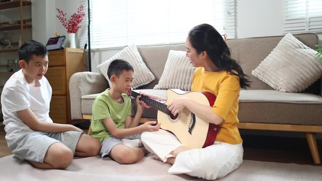 Mother teaching music to her children while playing guitar at home