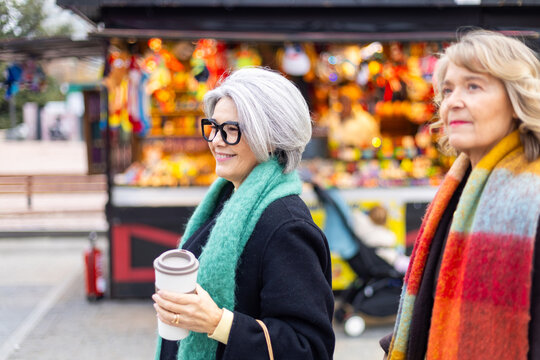 Mature women friends walking city street drinking coffee