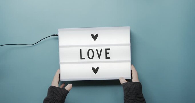 Person holding a light box that says love surrounded by red paper hearts hands lightbox message sign romance