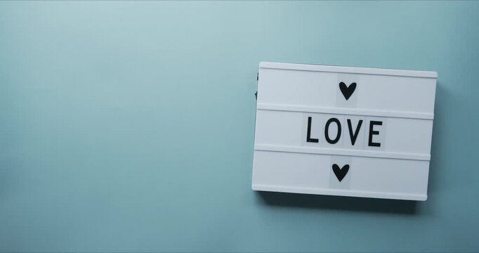 Illuminated cinema light box with the word love and heart icons on light blue surface lightbox sign message romance