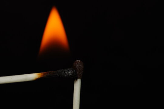 Extreme close-up macro photograph of a burning match surrounded by a large vivid orange and yellow flame against black.