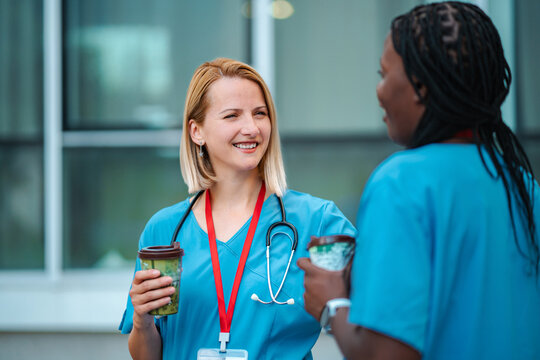 Two female nurses enjoying a coffee break outside, smiling and talking