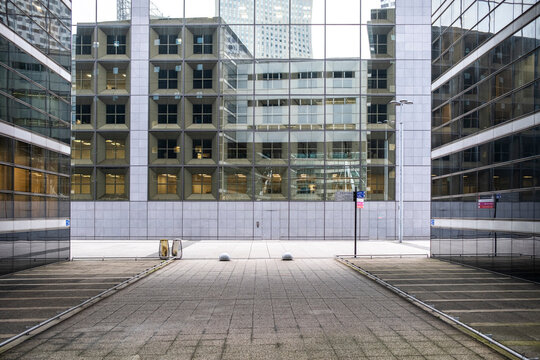 A corporate facade anchors an empty office courtyard as architecture encloses the plaza between business buildings in a symmetrical urban setting