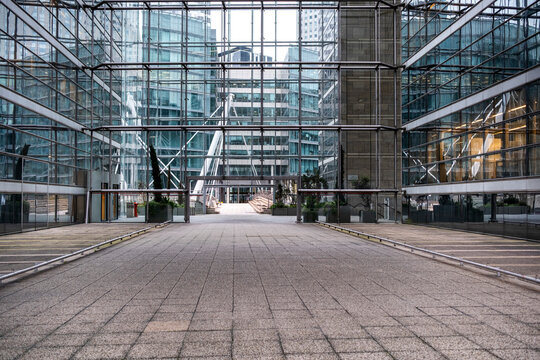 An empty office plaza opens between corporate buildings, where a glass walkway crosses the business complex and architecture shapes this urban pedestrian space