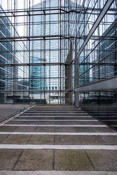 A glass atrium frames an empty office walkway where corporate architecture surrounds a pedestrian plaza in an urban business complex defined by structural lines