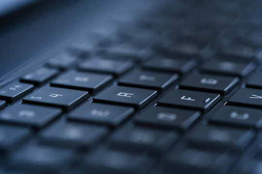 Macro view of black laptop keyboard keys with shallow depth of field and blue lighting