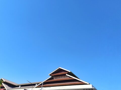 Roof of a traditional Indonesian building with ornate wooden carvings set against a clear blue sky