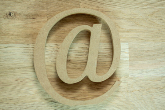A simple wooden at symbol rests on a textured wood background
