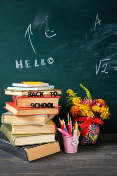 back to school concept. stationery, flowers bouquet and stack of learning books close up on table against chalkboard. symbol of beginning of the school year, Knowledge Day, education,1 September