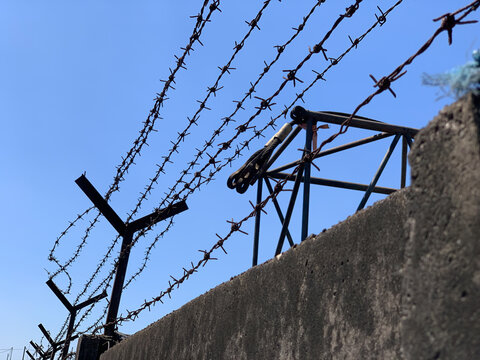 Rusty barbed wire on a vintage metal fence post against a clear blue sky. Symbolic image of border security, prison, human rights, and historical memory
