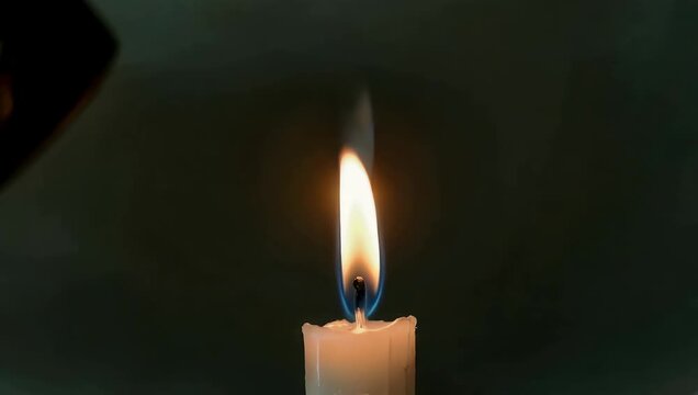 Dramatic 4K slow-motion clip showing a gust of wind nearly extinguishing a burning candle flame creating a flickering dance of light inside a peaceful dark room
